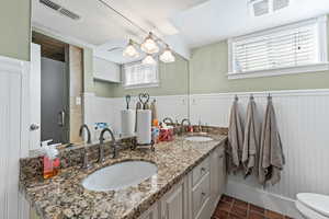 Bathroom featuring double vanity, dark tile patterned flooring, a shower stall, and a wainscoted wall