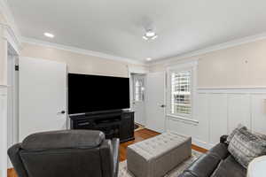 Living room with wood finished floors, crown molding, a decorative wall, wainscoting, and recessed lighting