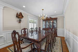 Dining space with a decorative wall, a wainscoted wall, ornamental molding, wood finished floors, and a chandelier
