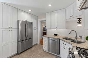 Kitchen with stainless steel appliances, white cabinetry, recessed lighting, light stone countertops, and extractor fan