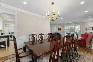 Dining space with wood finished floors, crown molding, recessed lighting, a chandelier, and wainscoting