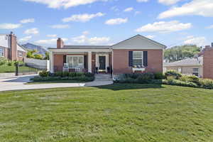 View of front of house with covered porch, brick siding, and a chimney