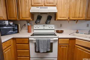 Kitchen with electric range, under cabinet range hood, light countertops, black microwave, and brown cabinetry
