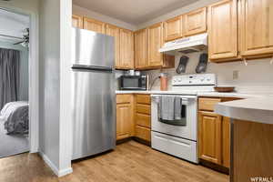 Kitchen with light countertops, white electric range, freestanding refrigerator, under cabinet range hood, and black microwave