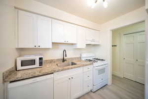 Kitchen with white appliances, white cabinetry, light wood-style floors, light stone counters, and under cabinet range hood