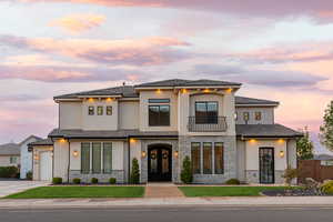 View of front facade with a balcony, stone siding, stucco siding, french doors, and driveway