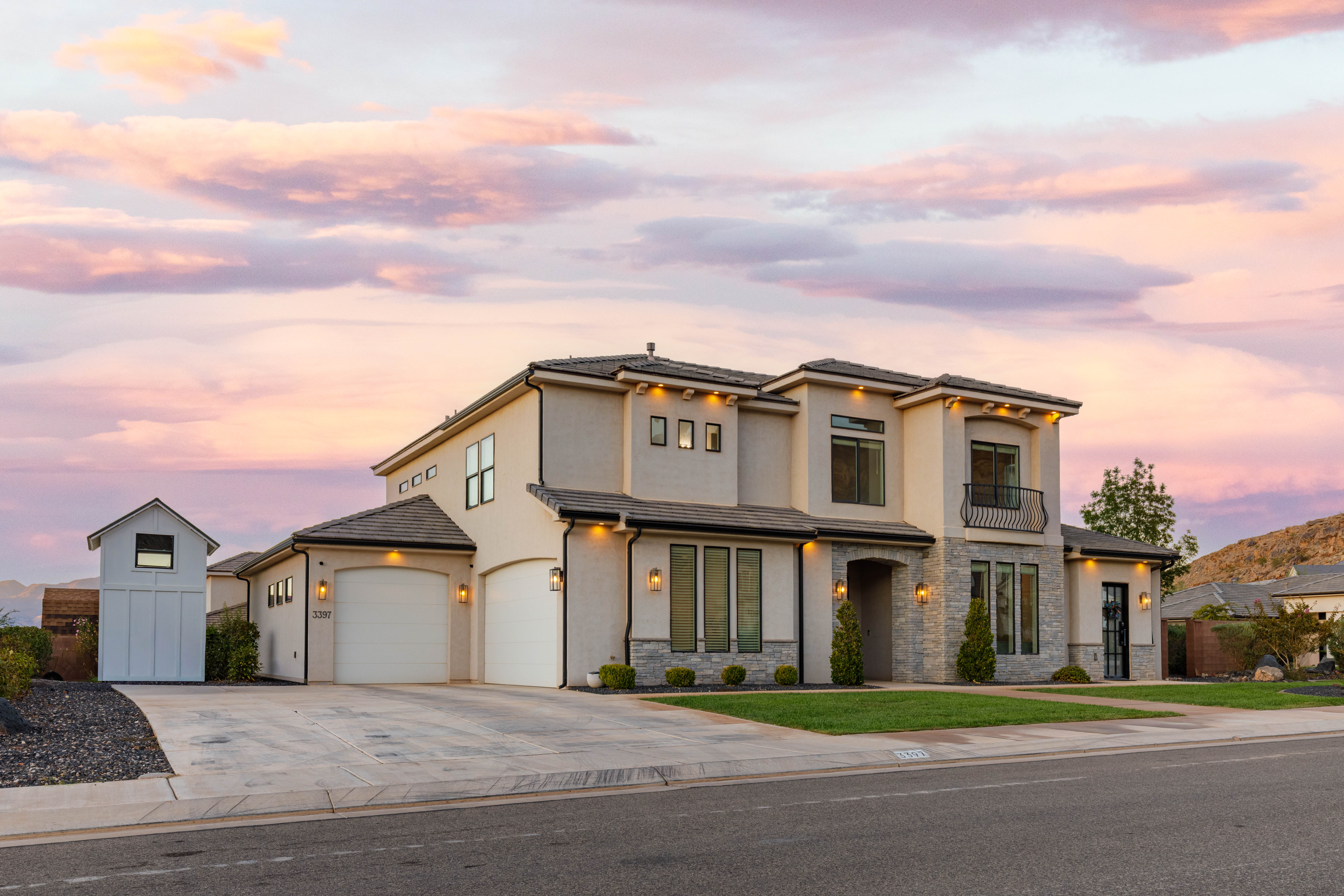 View of front facade featuring driveway, a balcony, stucco siding, stone siding, and a front lawn