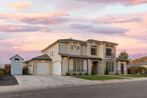 View of front facade featuring driveway, a balcony, stucco siding, stone siding, and a front lawn