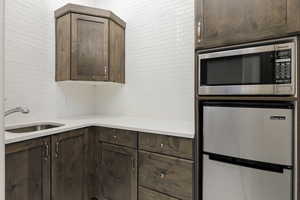 Kitchen featuring stainless steel appliances, dark brown cabinets, light stone counters, and tasteful backsplash