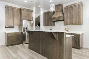 Kitchen featuring decorative light fixtures, stainless steel refrigerator with ice dispenser, light wood finished floors, recessed lighting, and a kitchen bar