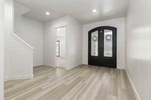 Entrance foyer featuring light wood finished floors, recessed lighting, french doors, stairs, and arched walkways
