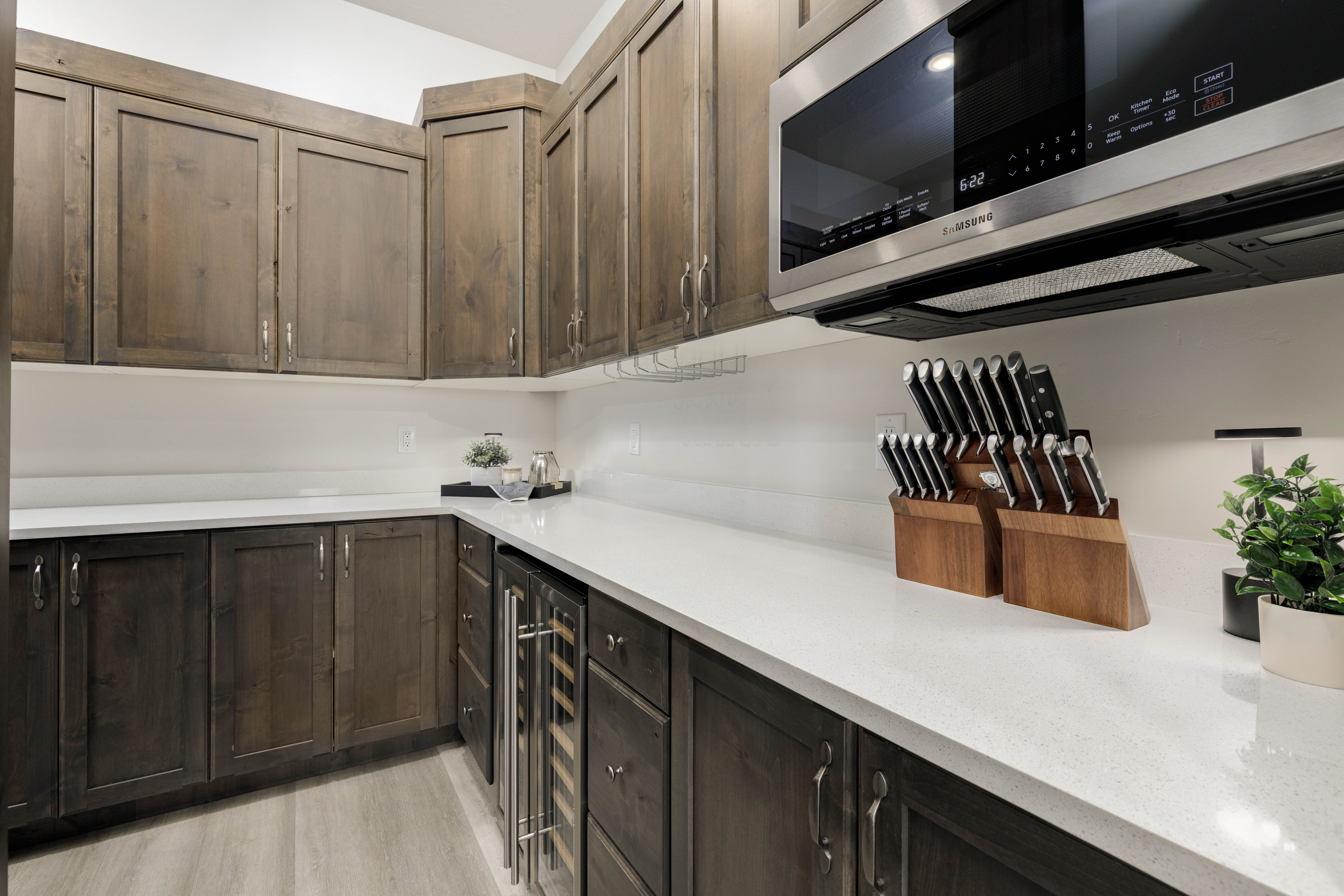Custom cabinetry in Butler Pantry featuring light wood finished floors, custom cabinetry, stainless steel microwave and quartz countertops for small appliances.