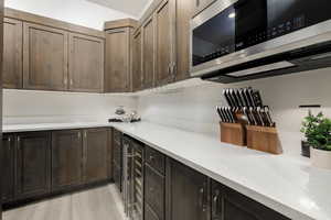 Custom cabinetry in Butler Pantry featuring light wood finished floors, custom cabinetry, stainless steel microwave and quartz countertops for small appliances.