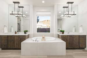 Owners Suite bathroom featuring two vanities, recessed lighting, light wood-type flooring, and a jetted tub