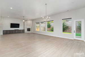 Unfurnished living room featuring a stone fireplace, a chandelier, a ceiling fan, light wood-style floors, and recessed lighting