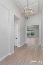 Front hallway looking into the living room. Featuring light wood-style floors, a towering ceiling, and a chandelier