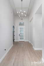 Entryway with light wood-type flooring, a chandelier, and a towering ceiling