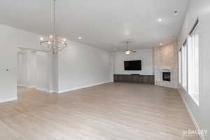 Unfurnished living room featuring ceiling fan, a fireplace, light wood-type flooring, a chandelier, and recessed lighting