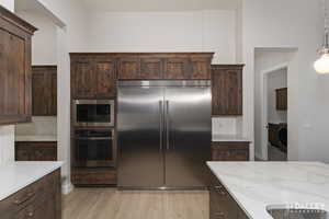 Kitchen featuring built in appliances, dark brown cabinets, light wood-style floors, light quartz countertops, and decorative light fixtures