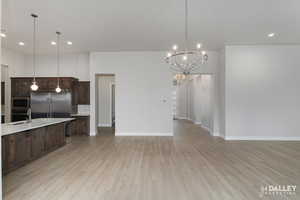 Kitchen and dining area with recessed lighting, dark brown cabinets, light wood-type flooring, a kitchen breakfast bar, and appliances with stainless steel finishes