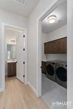 Washroom with washing machine and dryer, light wood-style flooring, and cabinet space