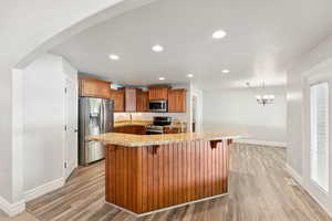 Kitchen with brown cabinets, appliances with stainless steel finishes, recessed lighting, arched walkways, and a kitchen breakfast bar
