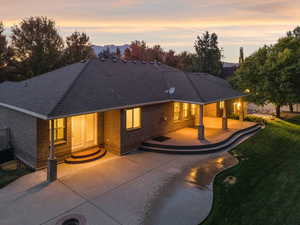 Rear view of house featuring roof with shingles, brick siding, a patio area, and a lawn