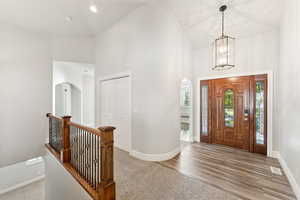 Carpeted entrance foyer featuring arched walkways, high vaulted ceiling, and wood finished floors