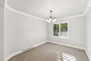 Carpeted empty room with ornamental molding and a chandelier