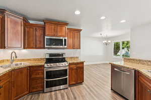 Kitchen with appliances with stainless steel finishes, light wood-type flooring, recessed lighting, brown cabinets, and hanging light fixtures
