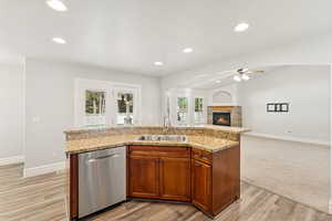 Kitchen with a center island with sink, a fireplace, dishwasher, vaulted ceiling, and brown cabinets
