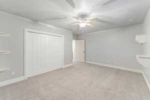 Unfurnished bedroom featuring light colored carpet, a closet, a ceiling fan, and a textured ceiling