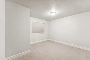Empty room with light colored carpet and a textured ceiling