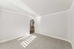 Carpeted empty room featuring arched walkways and ornamental molding