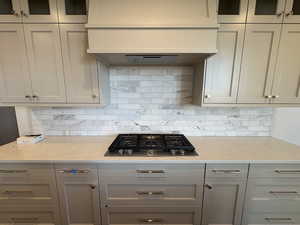 Kitchen featuring under cabinet range hood, light stone counters, glass insert cabinets, and backsplash
