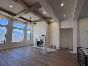 Unfurnished living room with a fireplace, coffered ceiling, beamed ceiling, ceiling fan, and dark wood-style floors