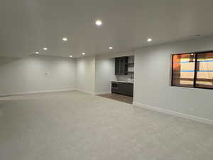 Below grade area featuring recessed lighting, light carpet, and bar with sink