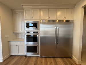 Kitchen with built in appliances, dark wood-style floors, tasteful backsplash, white cabinets, and light stone countertops