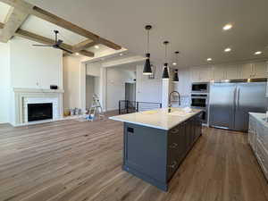 Kitchen featuring built in appliances, beamed ceiling, decorative light fixtures, open floor plan, and dark wood-style flooring