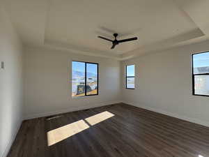 Empty room with a raised ceiling, dark wood-style flooring, and a ceiling fan