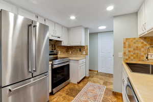 Kitchen with stainless steel appliances, white cabinetry, light countertops, under cabinet range hood, and recessed lighting