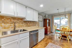 Kitchen with light countertops, white cabinets, backsplash, stainless steel dishwasher, and pendant lighting