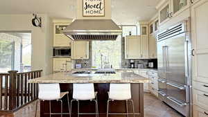 Kitchen featuring glass insert cabinets, backsplash, light stone counters, built in appliances, and a kitchen island