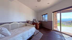 Bedroom featuring dark wood-style floors, access to exterior, wainscoting, and vaulted ceiling