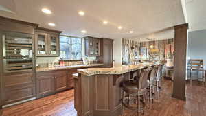 Bar area with glass insert cabinets, dark wood-style flooring, recessed lighting, a textured ceiling, and light stone counters
