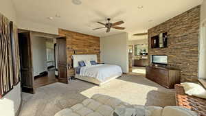 Bedroom featuring light carpet, wooden walls, ensuite bath, and a ceiling fan