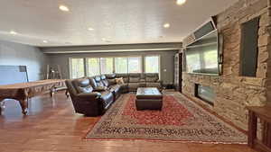 Living area featuring a textured ceiling, recessed lighting, billiards, wood finished floors, and a stone fireplace