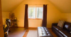 Guest room with fold out couch featuring wood finished floors and vaulted ceiling