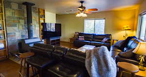 Living area with a wood stove, wood finished floors, built in shelves, and a ceiling fan