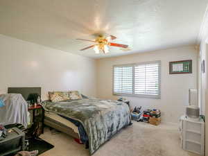 Carpeted bedroom featuring a textured ceiling, crown molding, and a ceiling fan